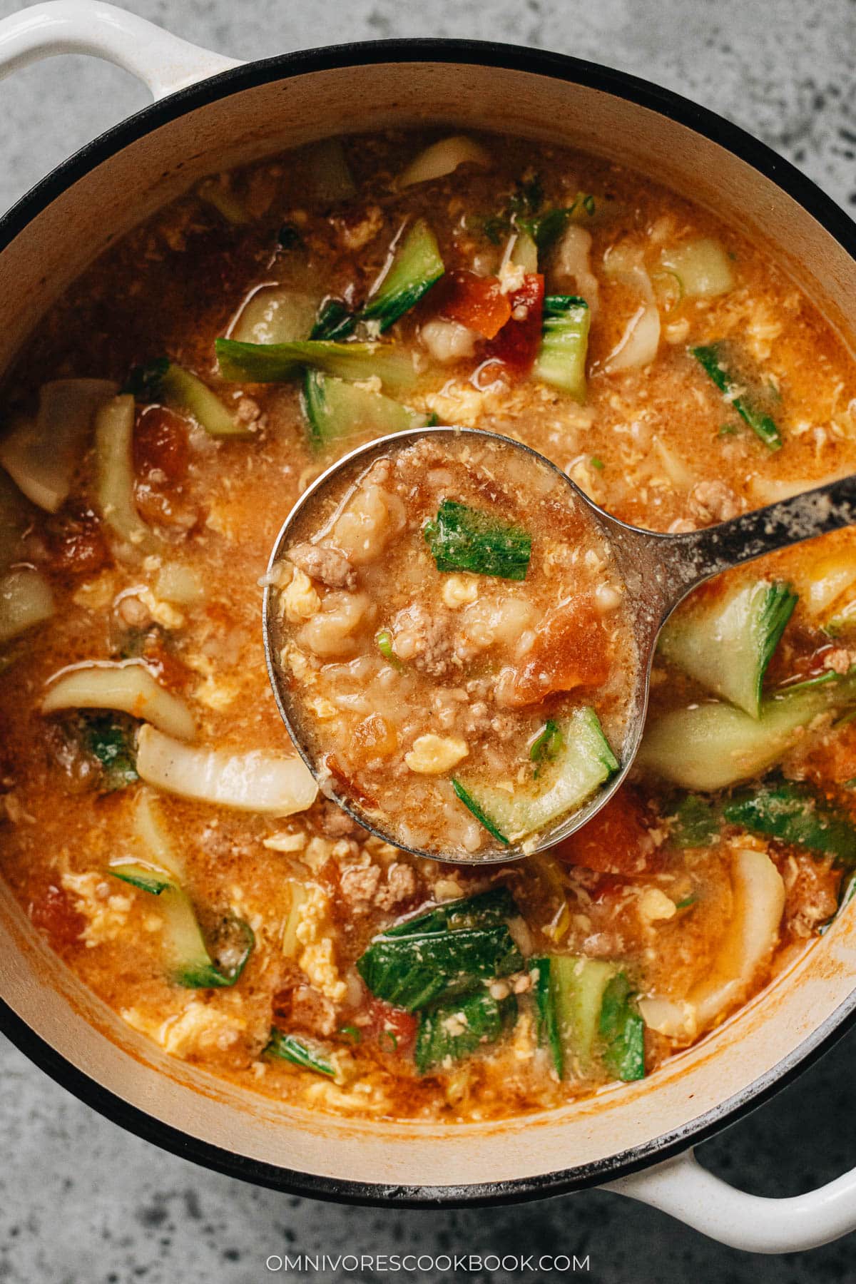 A ladle lifting a scoop of Ge Da Tang from a Dutch oven.
