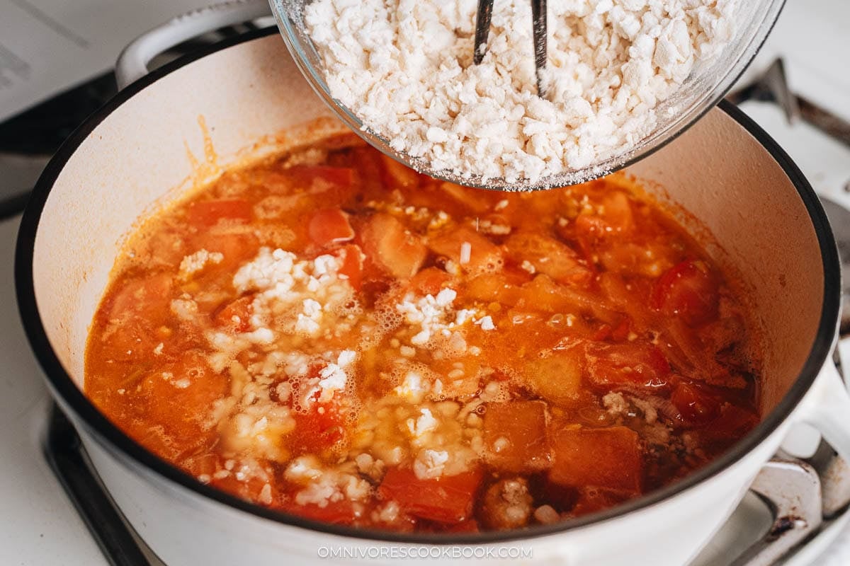 A bowl of dough drops being added into a simmering tomato broth.