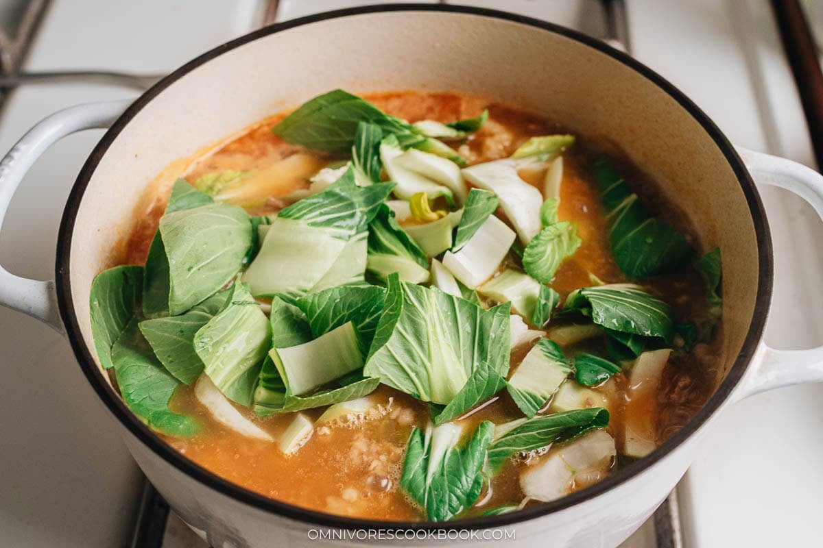 Freshly chopped bok choy added to a simmering broth in a Dutch oven.