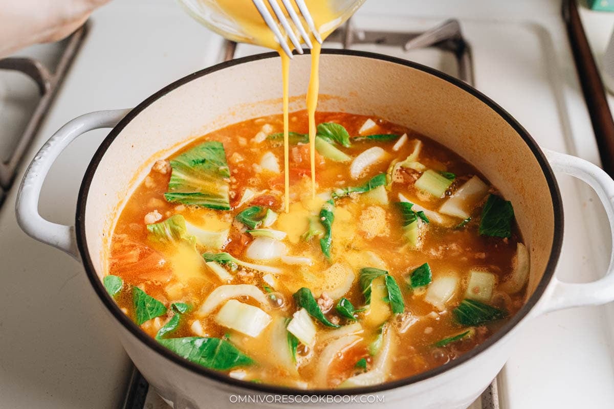 Beaten eggs being slowly drizzled into the bubbling pot of Ge Da Tang, creating silky egg ribbons.