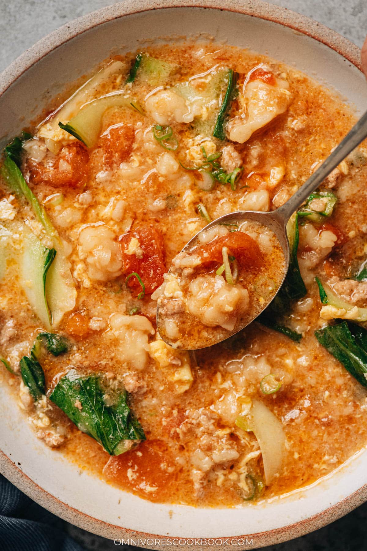 A close-up of Ge Da Tang in a bowl with a spoon lifting a piece of dough, showing the hearty texture of the soup and vegetables.