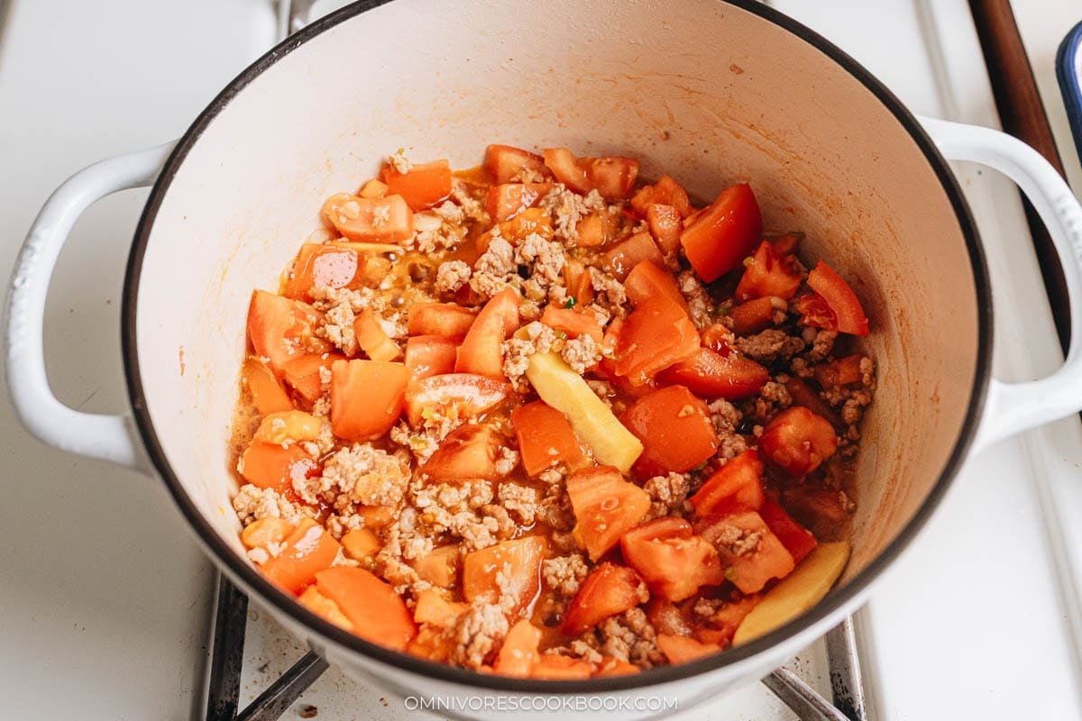 Chopped tomatoes simmering with browned pork and ginger in a Dutch oven to form the soup base.