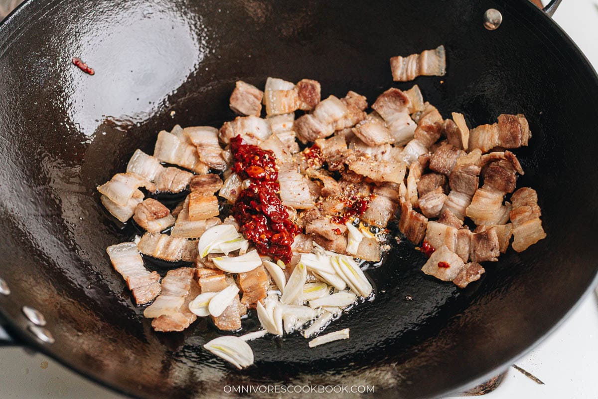 Pork belly slices in a wok with garlic, doubanjiang, and Sichuan peppercorns added to the center.