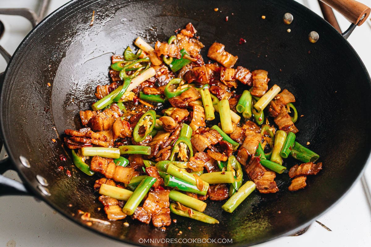 Twice cooked pork simmering in the wok with glossy red oil, caramelized pork belly, softened green onions, and sliced peppers evenly mixed.