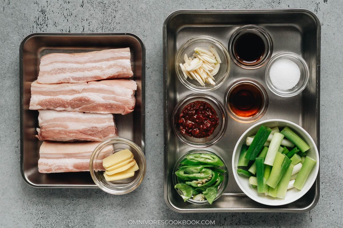 Prep tray with raw pork belly slabs, sliced ginger, chopped green onions, sliced peppers, garlic, doubanjiang, Shaoxing wine, soy sauce, and sugar arranged in bowls.