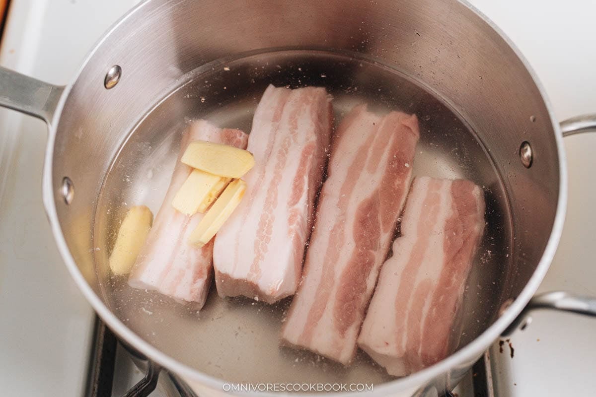 Pork belly and ginger slices simmering in a pot of water on the stovetop.
