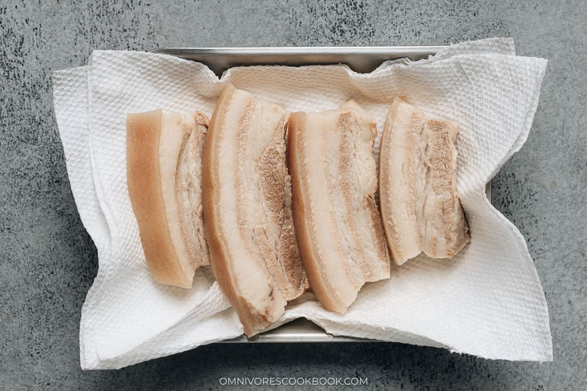 Cooked pork belly pieces draining on a tray lined with paper towels.