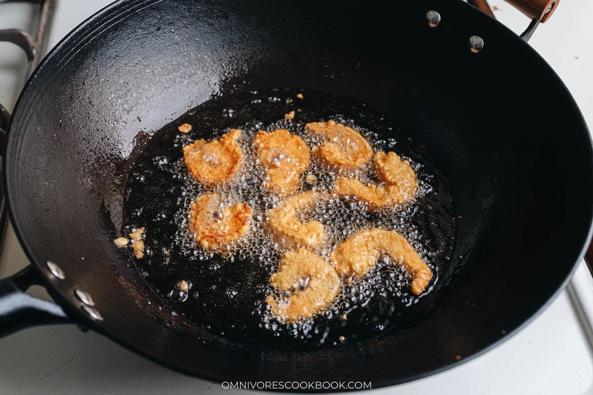 Shrimp frying in hot oil in a wok, forming a golden crispy coating.