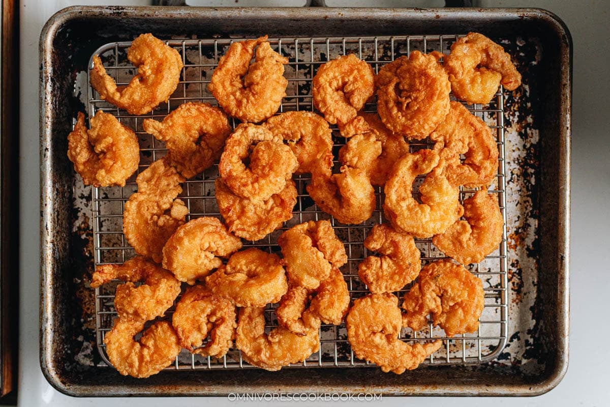 Freshly fried golden shrimp resting on a wire rack.