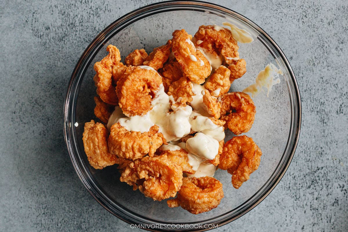 Fried shrimp being tossed with creamy wasabi mayo sauce in a glass bowl.