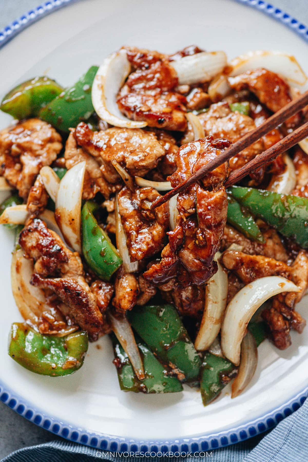 Chopsticks picking up a piece of pork from the stir fry