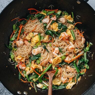 Shrimp mei fun stir fried in a wok with shrimp, egg, carrots, and choy sum.