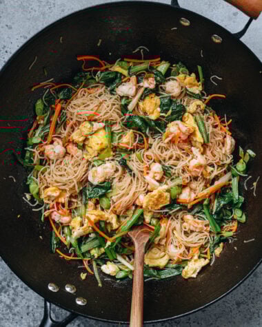 Shrimp mei fun stir fried in a wok with shrimp, egg, carrots, and choy sum.
