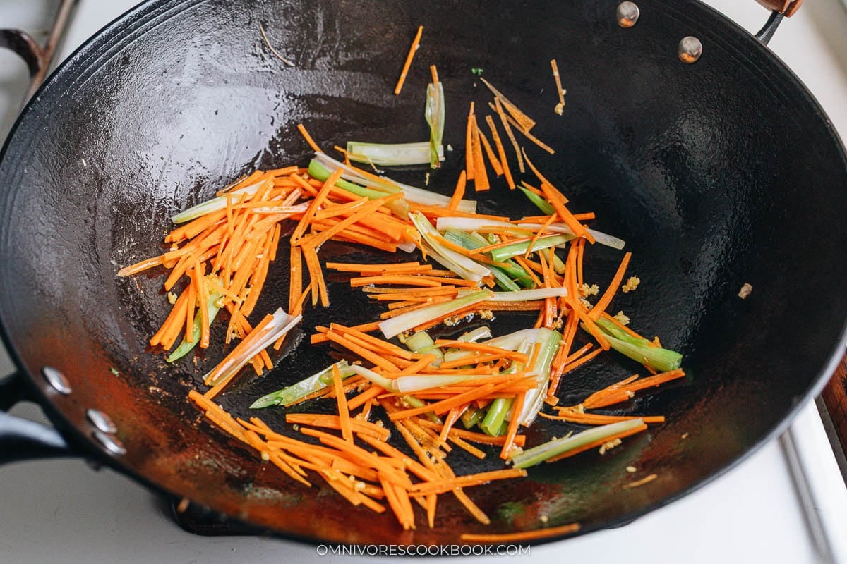 Cooking julienned carrots and scallions in a wok.