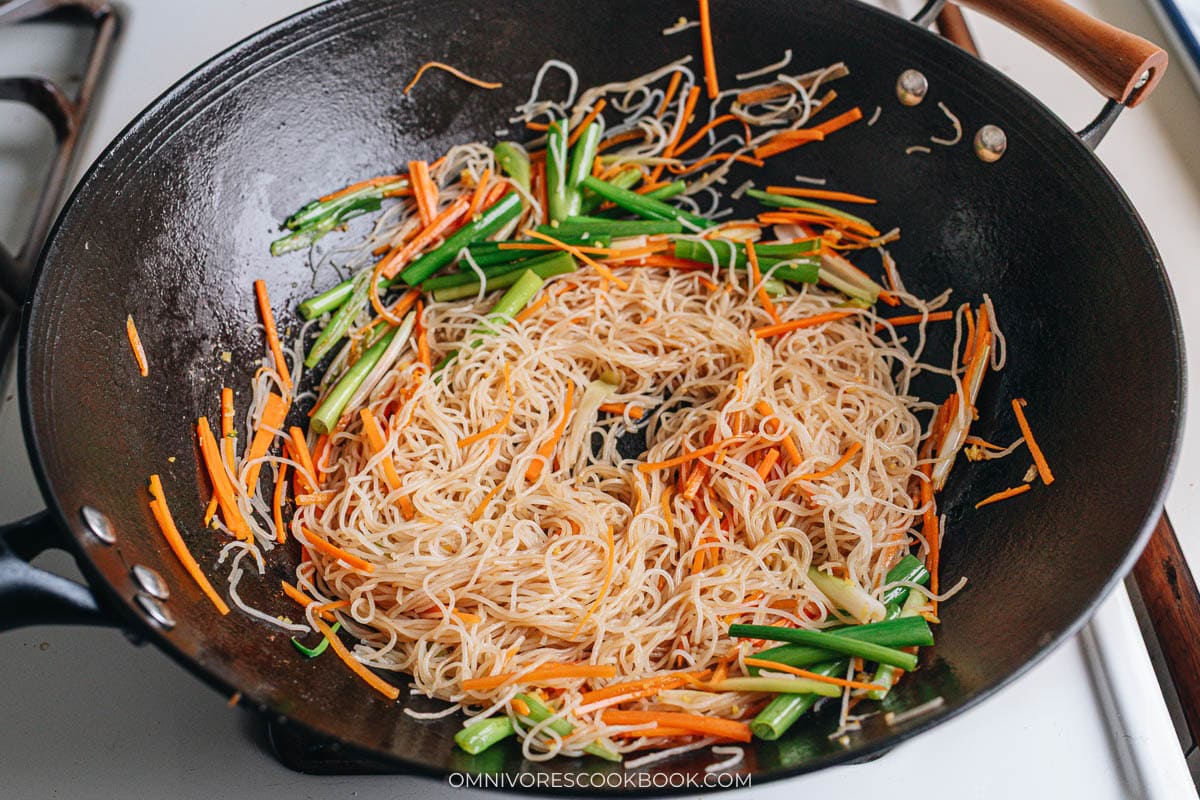 Adding rice vermicelli noodles into the wok with vegetables.