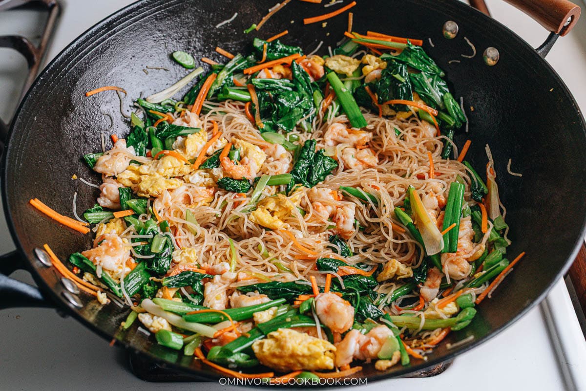 Stir frying shrimp mei fun with shrimp, eggs, and vegetables in a wok.