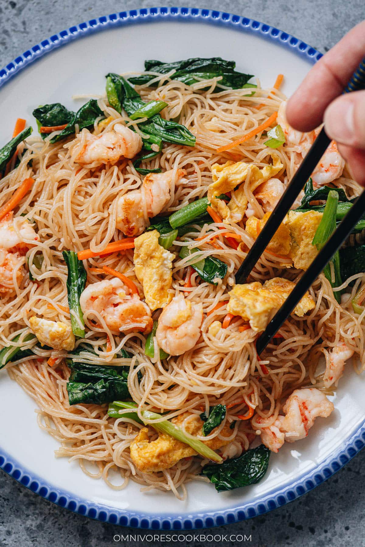 Plate of shrimp mei fun with chopsticks picking up noodles