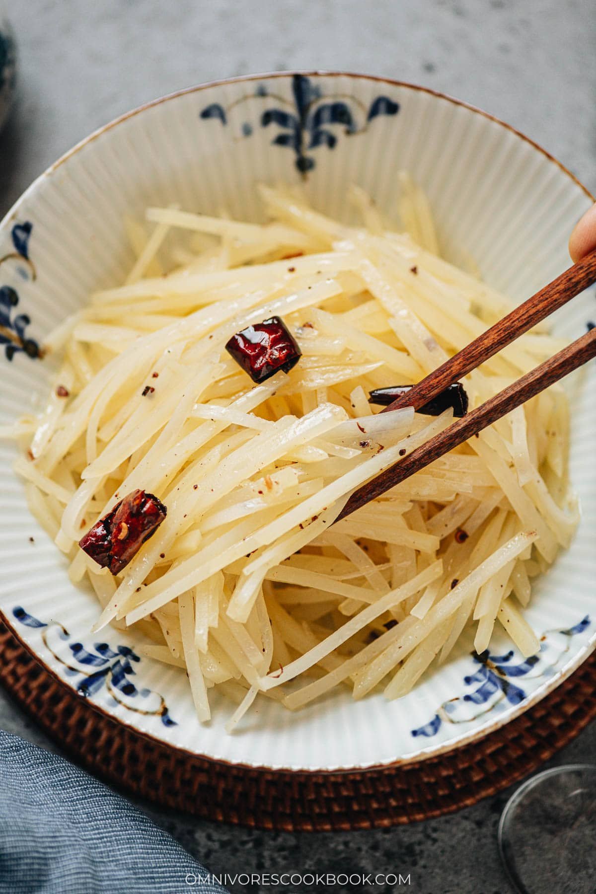 Chopsticks lifting julienned potatoes from Chinese potato salad