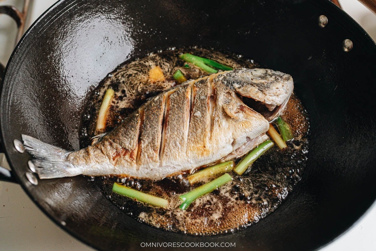Royal dorade simmering in soy sauce braising liquid in wok