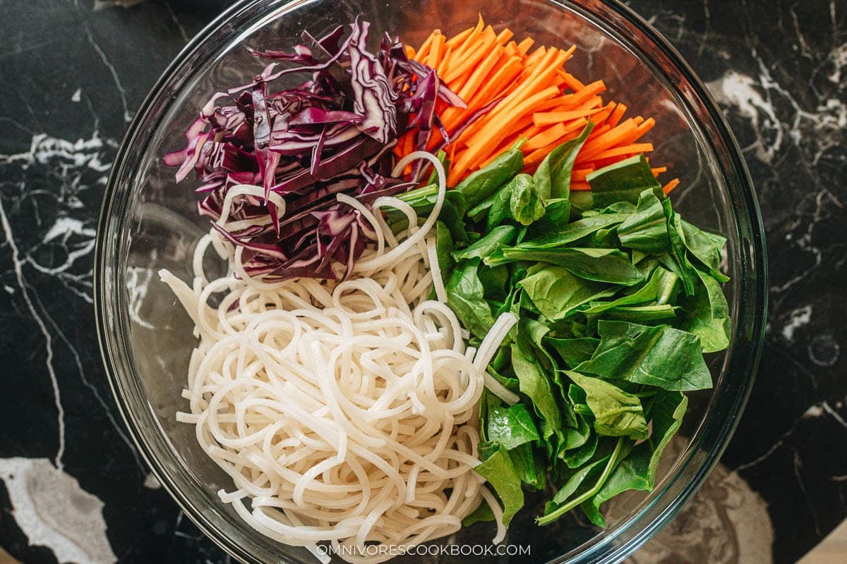 Shred the cabbage, chop the spinach, and shred the carrot all in a large bowl