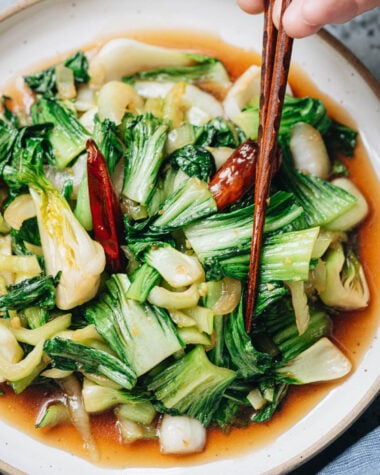 Chopsticks lifting bok choy coated in oyster sauce