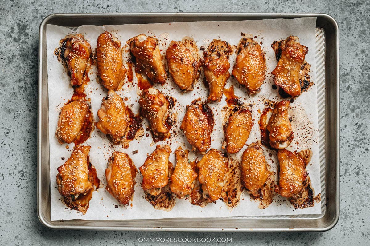 Chinese Baked crispy chicken wings on a baking sheet with sesame seeds.