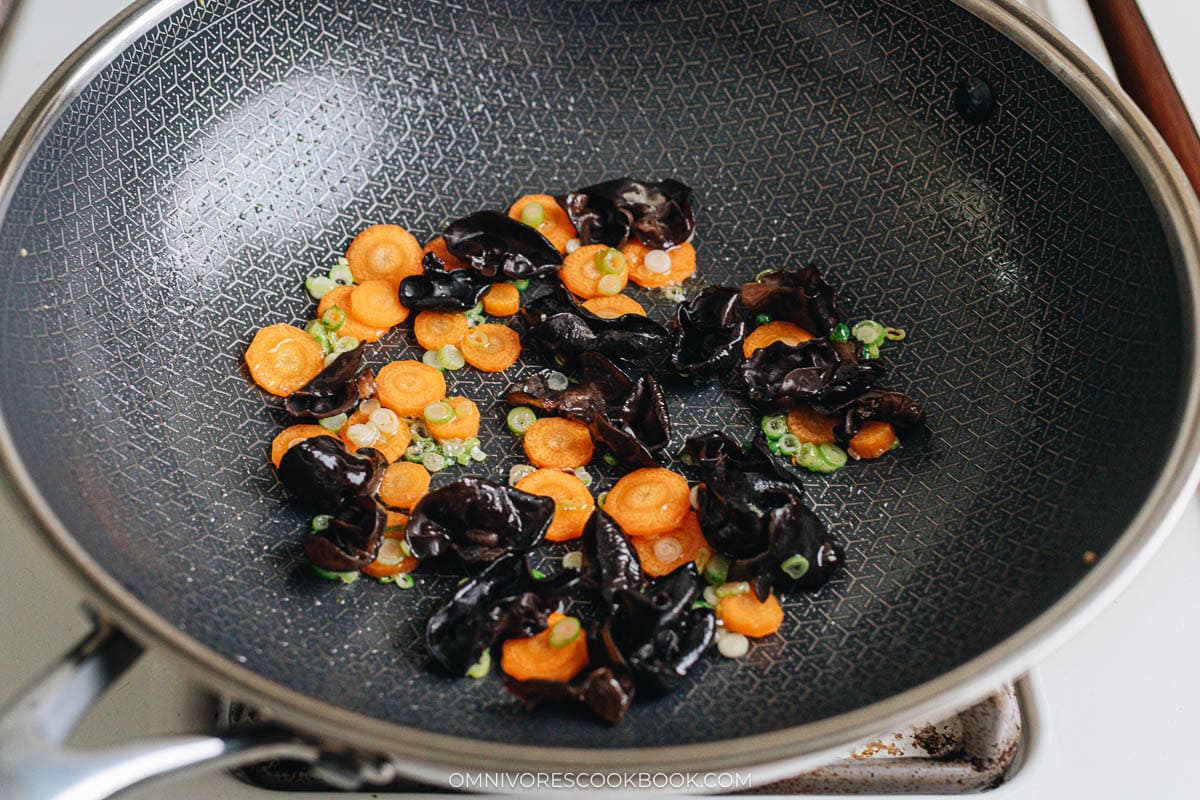 Stir frying wood ear mushrooms, carrots, and scallions in a wok