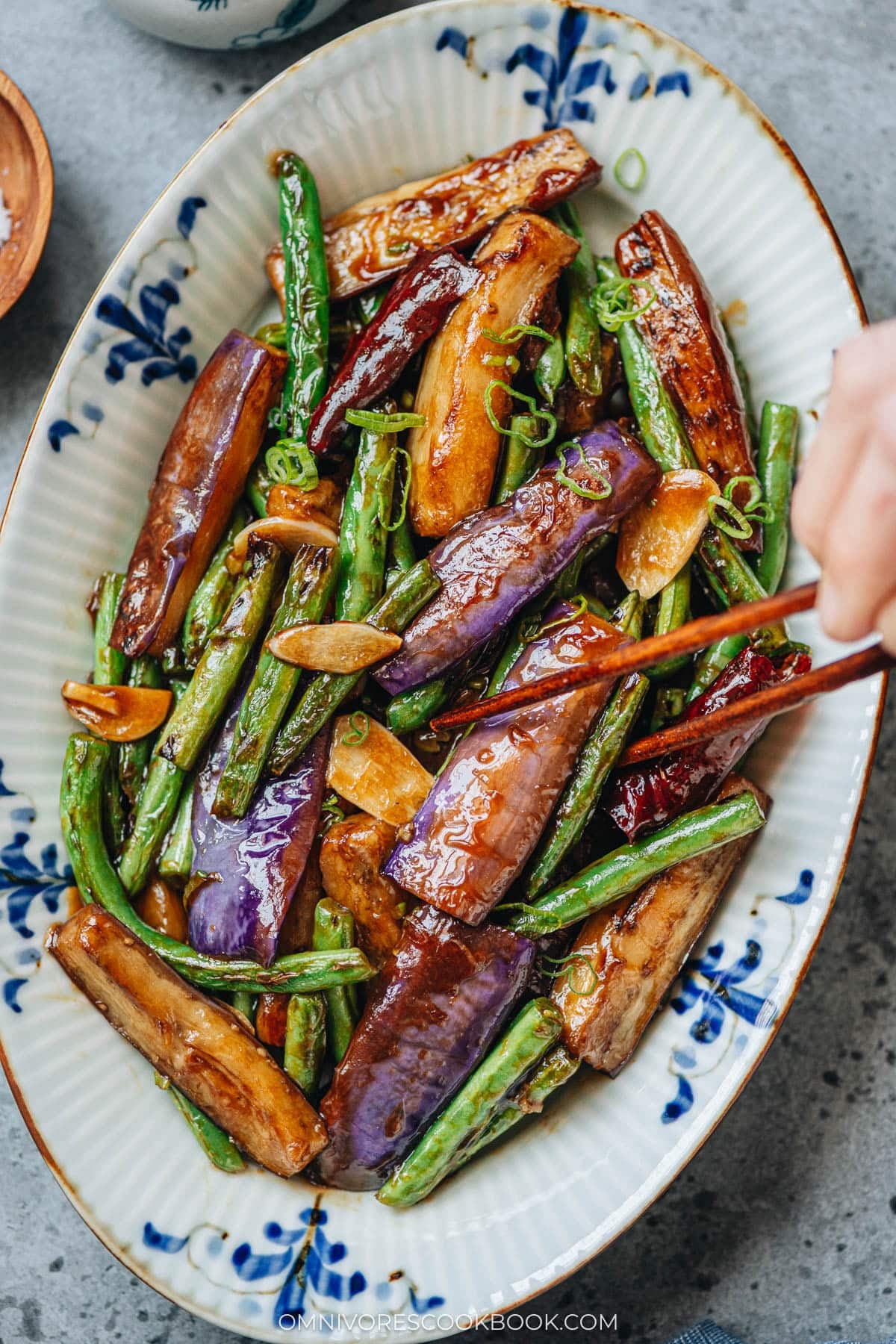 Chopsticks picking up stir fried eggplant and green beans
