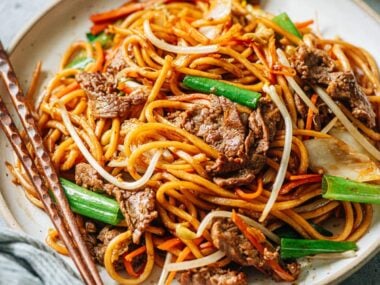 A plate of stir-fried Asian style noodles with chopsticks