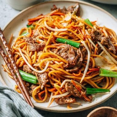 A plate of stir-fried Asian style noodles with chopsticks