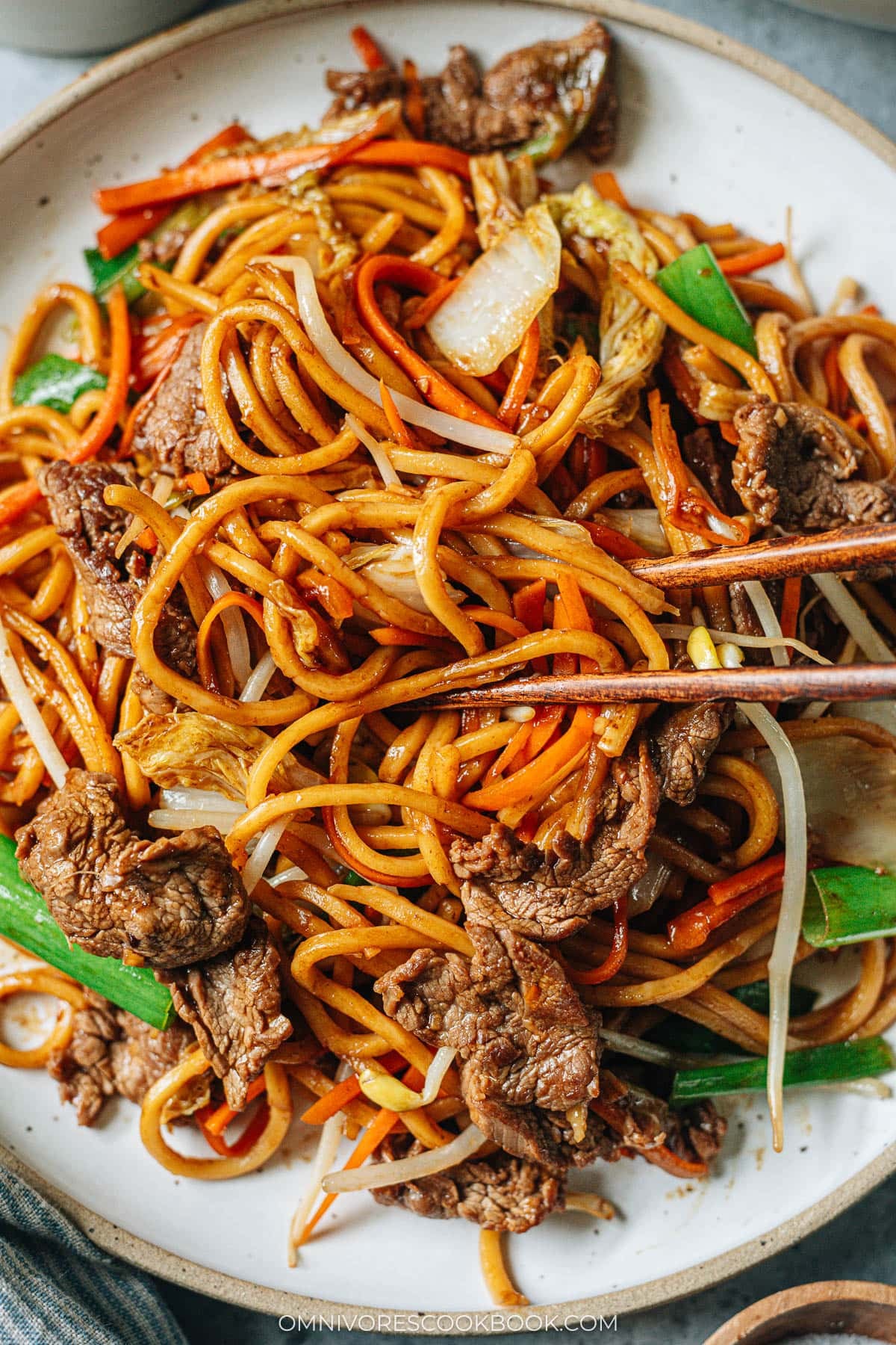 Closeup of chopsticks grabbing a bite of beef lo mein