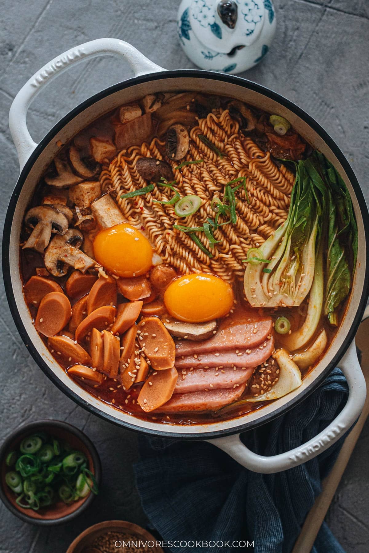 Korean Army Stew (Budae Jjigae) - Rich spicy broth made with aromatics, ground meat, and noodles, topped with sausage, veggies and runny egg yolks. An easy one-pot meal that requires very little prep and is fast to make. Korean army stew in a pot