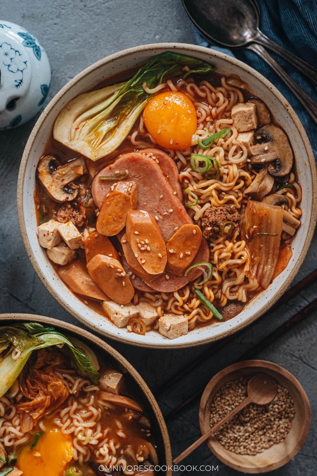 Korean Army Stew (Budae Jjigae) - Rich spicy broth made with aromatics, ground meat, and noodles, topped with sausage, veggies and runny egg yolks. An easy one-pot meal that requires very little prep and is fast to make. Budae Jjigae served in bowls