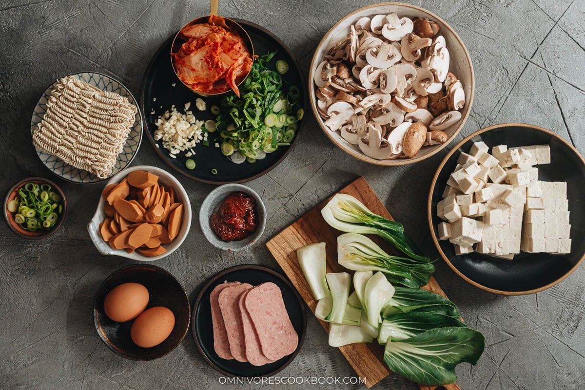 Korean Army Stew (Budae Jjigae) - Rich spicy broth made with aromatics, ground meat, and noodles, topped with sausage, veggies and runny egg yolks. An easy one-pot meal that requires very little prep and is fast to make. Budae Jjigae ingredients