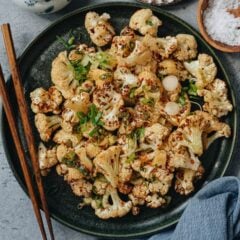 Roasted cauliflower with green onions on a black plate, garnished with chopped green onions.