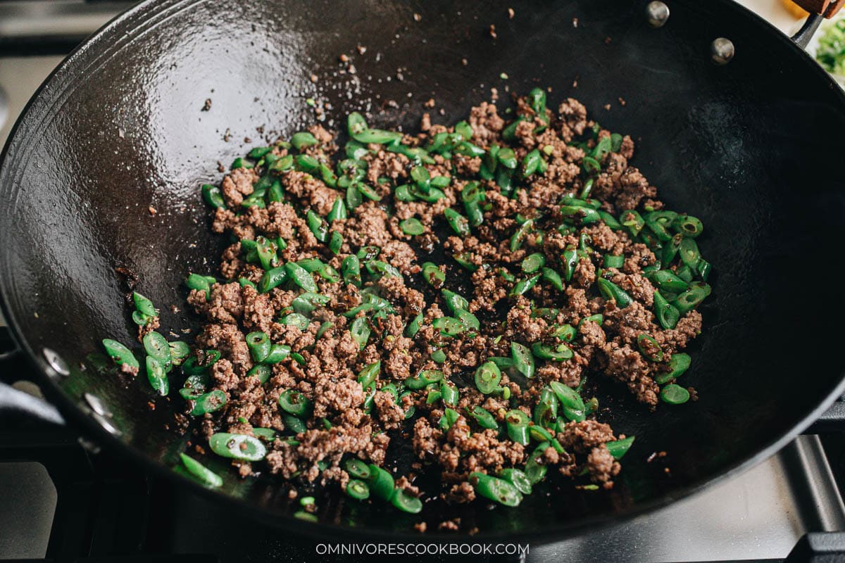 Ground beef, green beans, and sui mi ya cai cooking in a wok