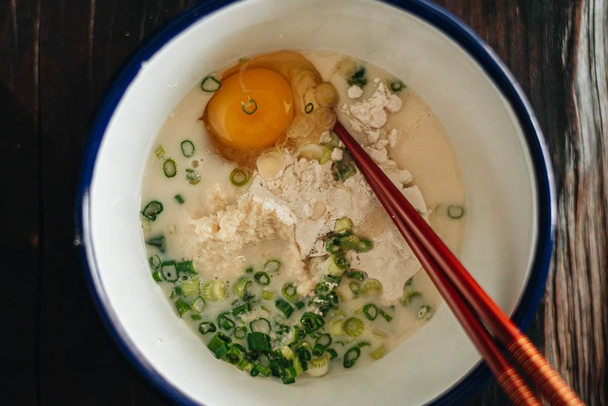 Okara, flour, egg, and green onion whisked into a smooth pancake batter in a bowl