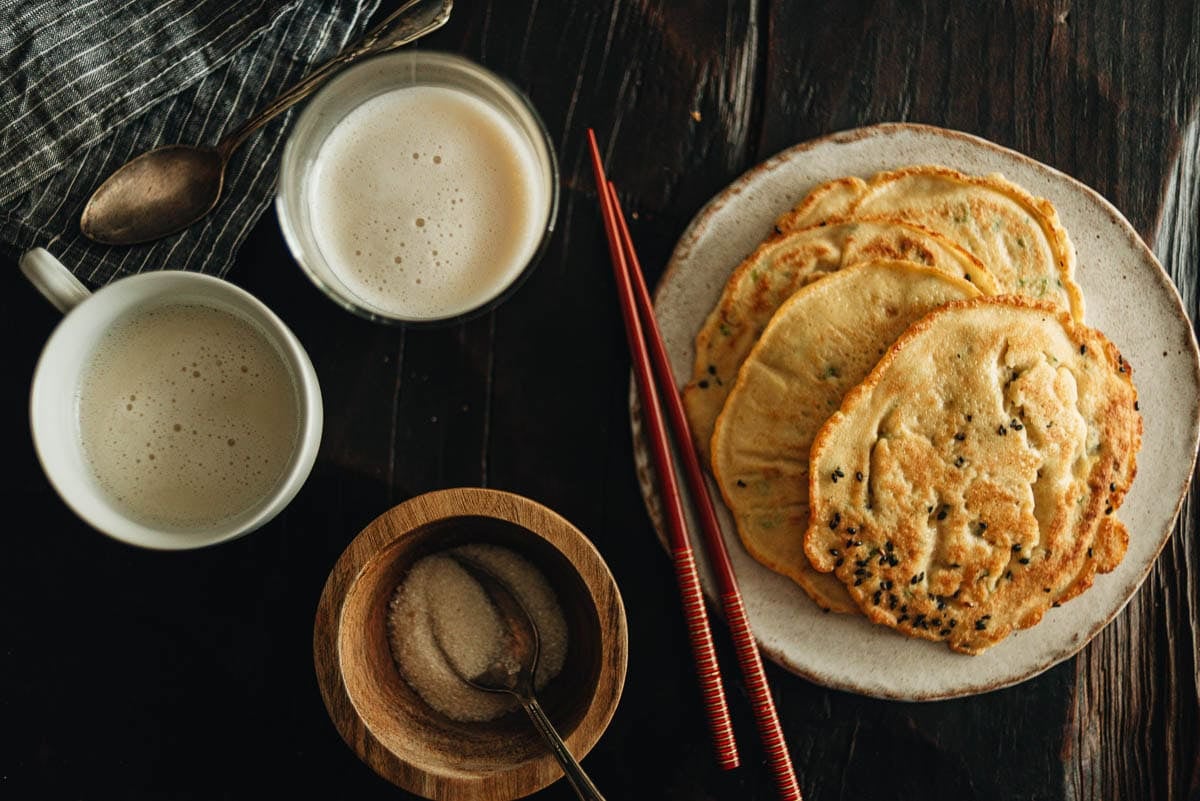 Finished okara pancakes on a plate next to a glass of homemade soy milk
