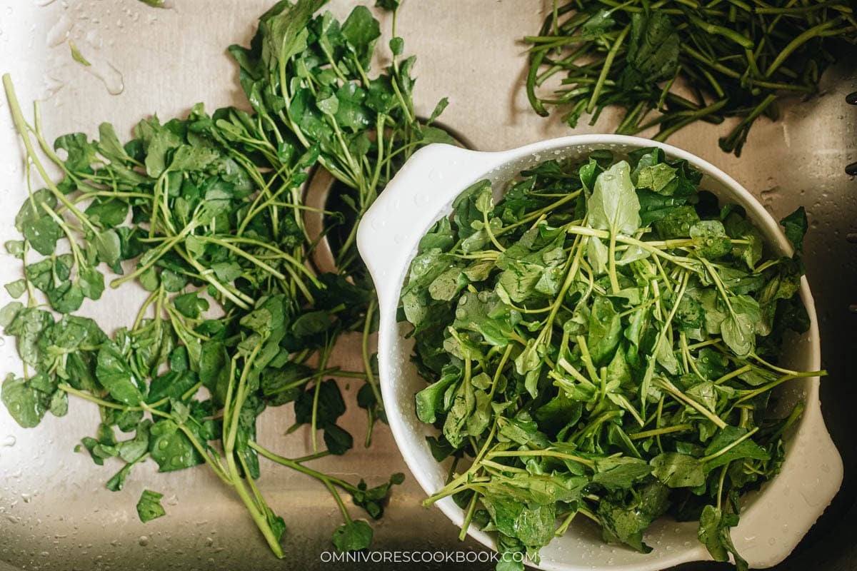 Hands pulling tough stems off fresh watercress leaves