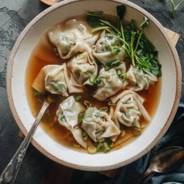 A bowl of wonton soup with pork and shrimp wontons, baby bok choy, and green onion in clear broth