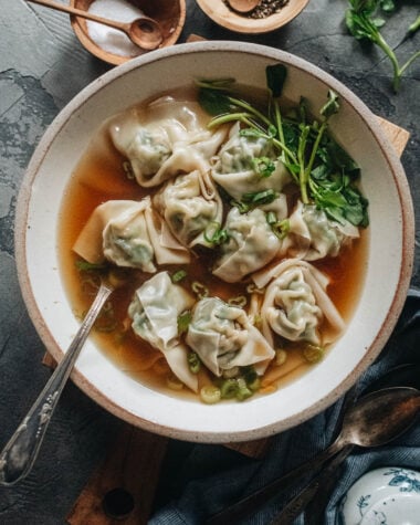 A bowl of wonton soup with pork and shrimp wontons, baby bok choy, and green onion in clear broth