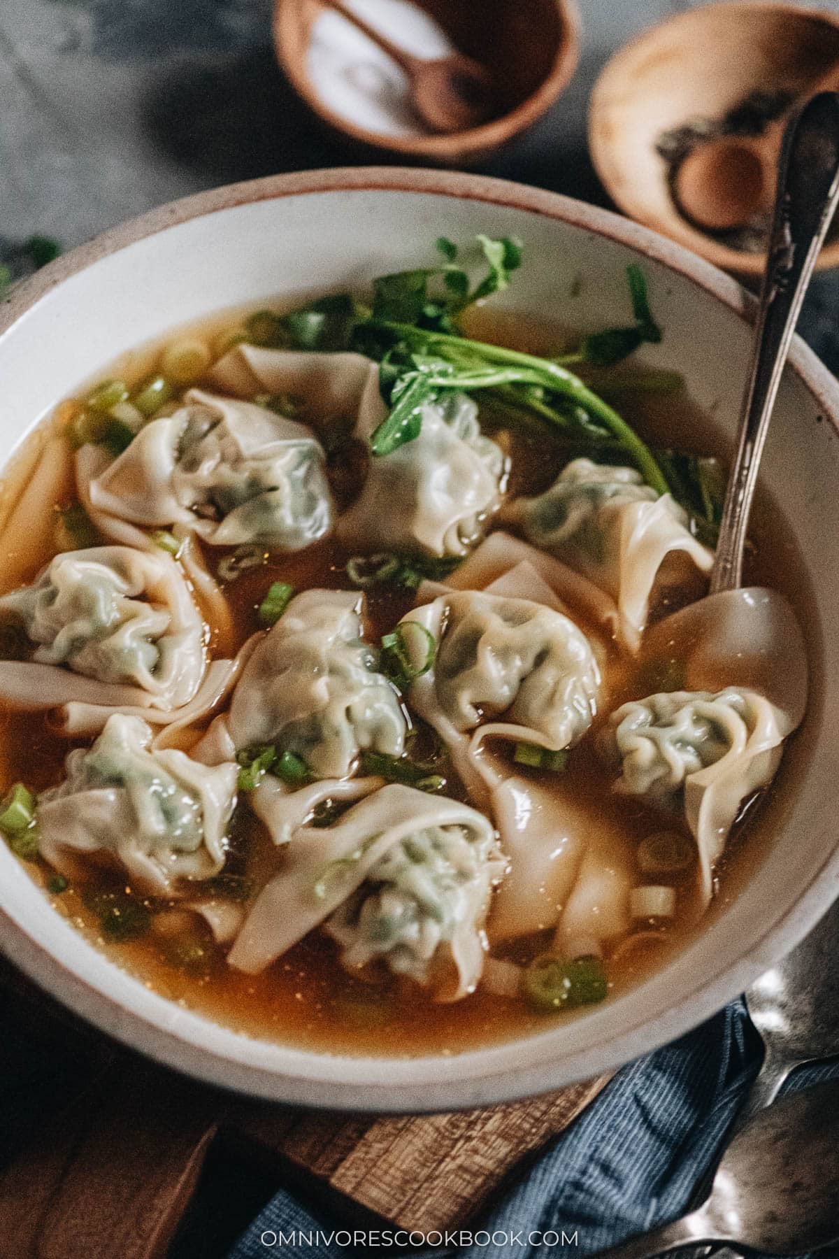 A bowl of wonton soup with pork and shrimp wontons, baby bok choy, and green onion in clear broth