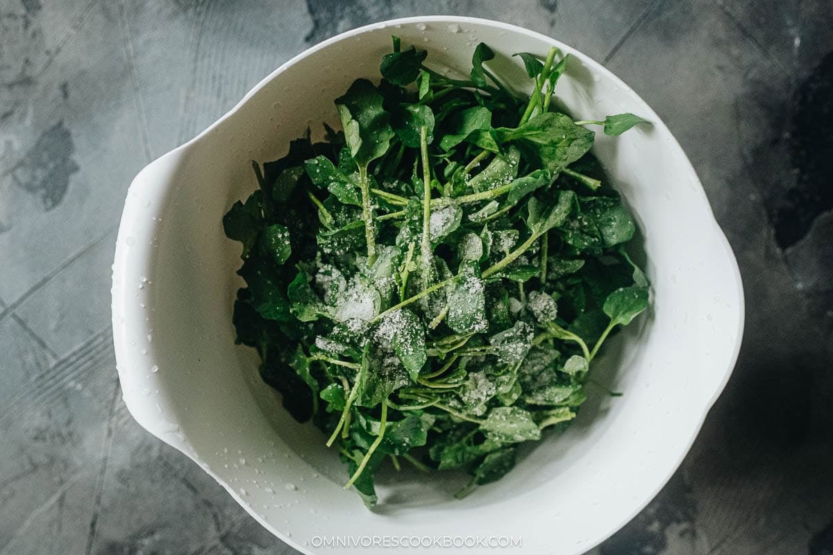 Salted watercress being squeezed by hand to press out water