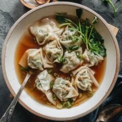 A bowl of wonton soup with pork and shrimp wontons, baby bok choy, and green onion in clear broth