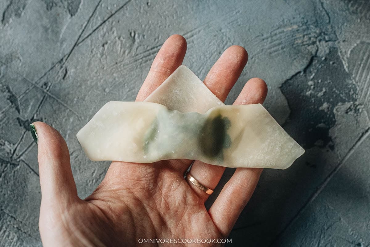 Fingers pressing a wet wonton wrapper closed to seal the watercress filling inside
