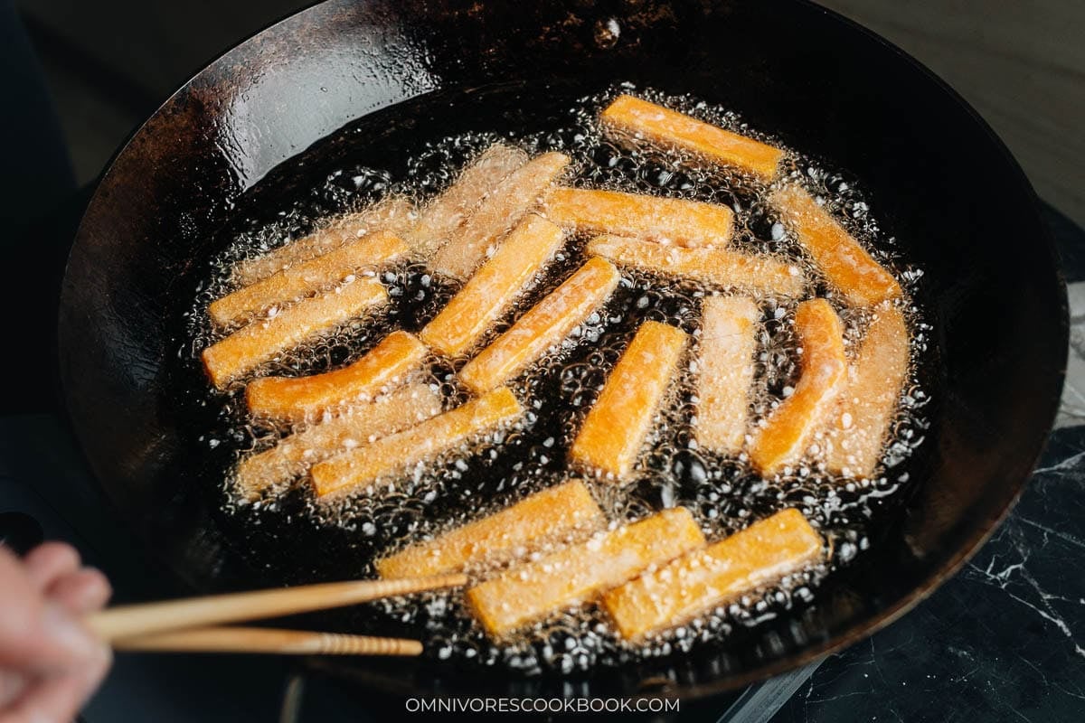 Cornstarch-coated pumpkin sticks shallow frying crisp in a hot skillet