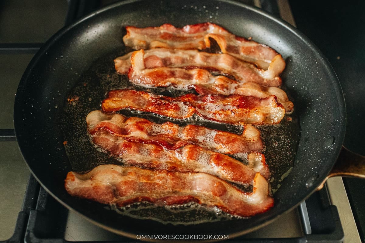 Thick cut bacon frying golden and crispy in a skillet 