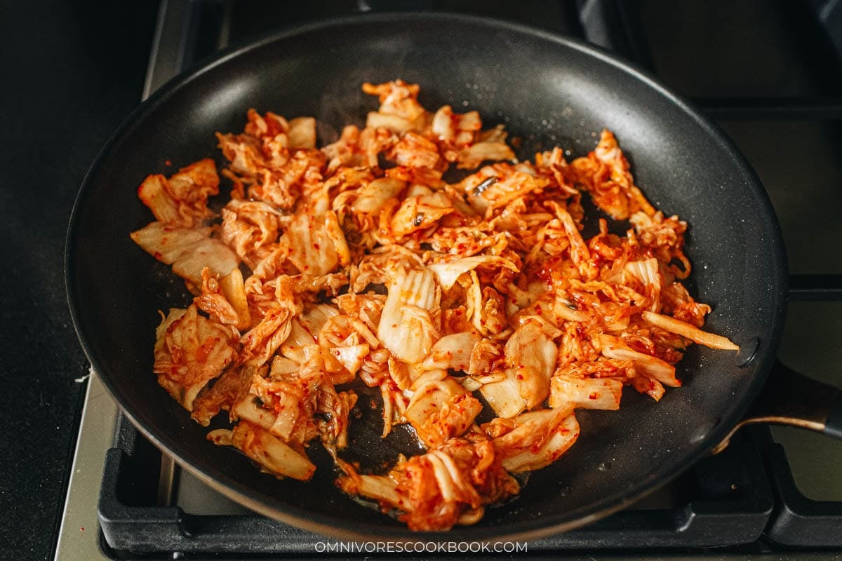 Chopped kimchi and thin kale stems cooking in peanut oil in a skillet
