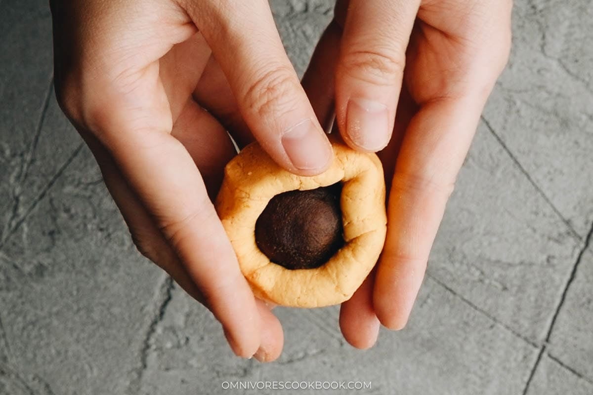 Wrapping pumpkin cake dough around red bean paste and pressing into a mini pancake