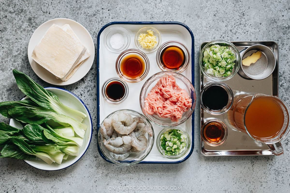 Wonton soup ingredients laid out: wonton wrappers, ground pork, shrimp, ginger, green onion, and bok choy